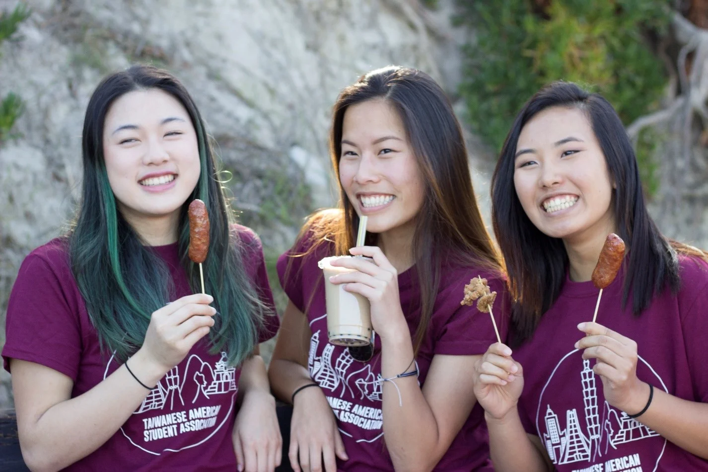   UCSB Students Lynn Tung, Katherine Tang, and Kelly Lam smile with sausages, boba milk tea, and popcorn chicken, all Taiwanese street food specialties.  