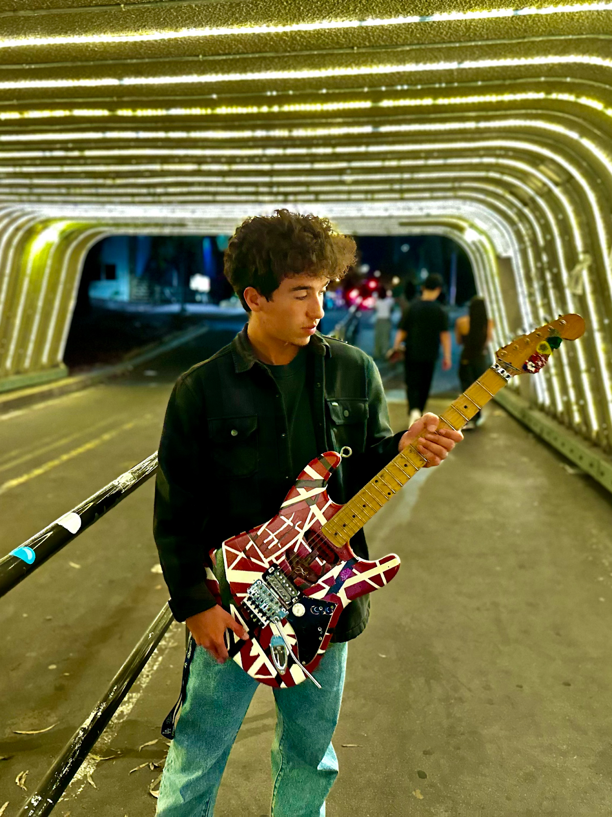  UCSB Music student Andrew Adorno holding his hand-built replica of Eddie Van Halen’s guitar under, the lights of Pardall Tunnel between UCSB and Isla Vista.  